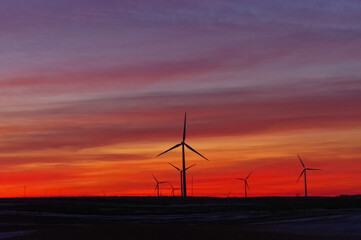 Turbiny wiatrowe na tle kolorowego nieba po zachodzie słońca.