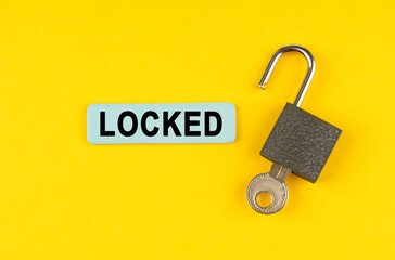 On the yellow surface lies an open lock with a key, next to it is a sticker with the inscription - locked