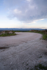 Road trip. View of the empty dirt road across the hills at sunset.