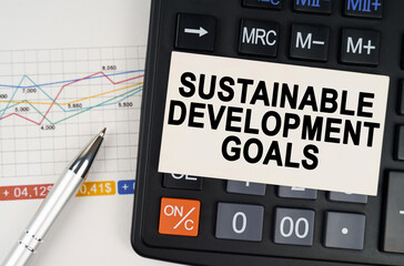 On the business chart lies a pen, a calculator and a business card with the inscription - Sustainable Development Goals
