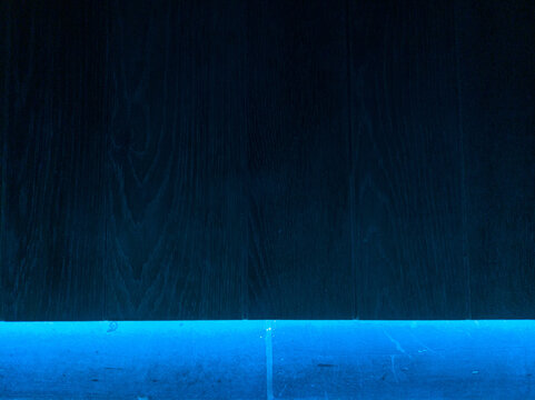 Oak, wooden wall illuminated from beneath by blue lighting, reflecting against bluestone border. Image taken in Herentals, Belgium.