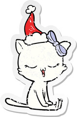 distressed sticker cartoon of a cat with bow on head wearing santa hat