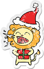 distressed sticker cartoon of a roaring lion with gift wearing santa hat