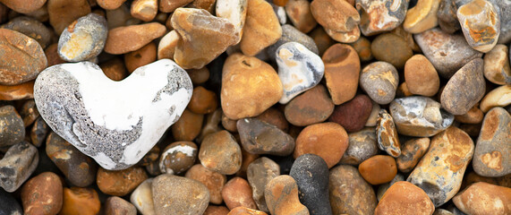 heart shaped white stone laying on pebble beach on the shore banner