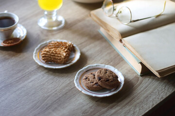Cup of tea, plates with cookies, glass of orange juice, books, reading glasses, bowl of fruit and candles on the table. Selective focus.