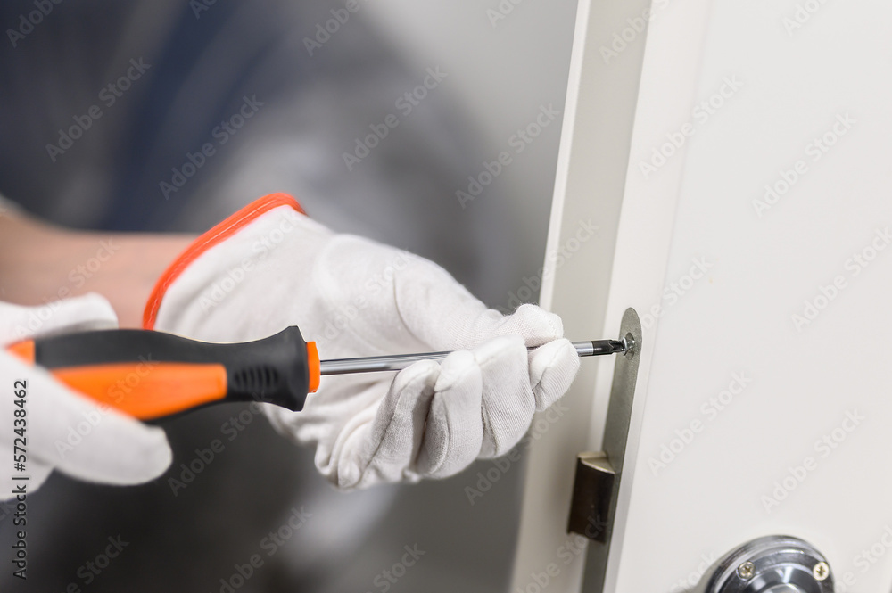 Wall mural men's hands with a manual screwdriver and a screw handle on a white door. door lock attachment.