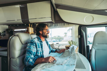 Happy mature man smilng inside a camper camping car using paper map guide to plan destinations...