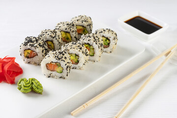 Sushi roll California with salmon, sesame seeds, avocado, cream cheese on white background. Sushi menu, rolls served on white dish and soy sauce. Traditional Japanese cuisine food.
