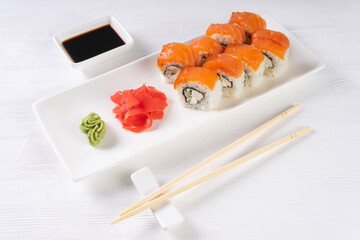 Sushi roll Philadelphia with salmon, smoked eel, avocado, cream cheese on white background. Sushi menu, rolls served on white dish with wasabi, ginger and soy sauce. Japanese cuisine food.