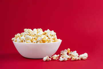 Scattered tasty cheese popcorn in white bowl isolated on red background. Flat lay, top view. Fast food, movie, cinema concept