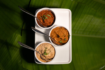 Three chutneys — ginger garlic chutney, tomato chutney, and peanut chutney — served fresh, against a backdrop of banana leaves.