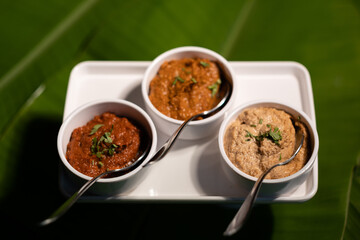 Three chutneys — ginger garlic chutney, tomato chutney, and peanut chutney — served fresh, against a backdrop of banana leaves.