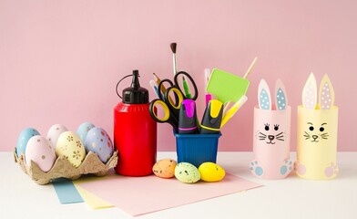 Cute, funny rabbits made of colored paper on a pink background.  Craft for the Easter holiday, Easter eggs and office supplies are on the table.  Easter bright holiday concept.  Front view.