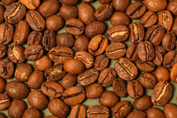 gros plan sur des grains de café posés sur un fond vert kaki, vue de dessus 

