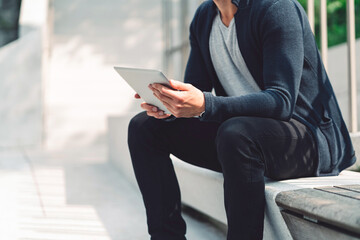 Unrecognizable man holding a digital tablet, sitting outside on a sunny day