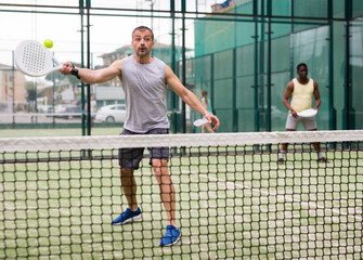 Male players playing padel in a padel court outdoor behind the net