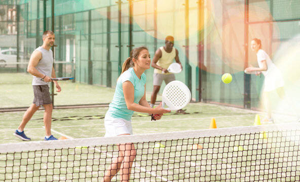 Portrait of cheerful woman paddle tennis player performing strokes technique at group training at court