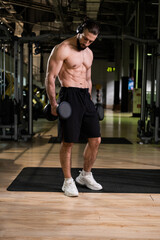 A muscular man with headphones does an exercise with dumbbells dumbbells in the gym