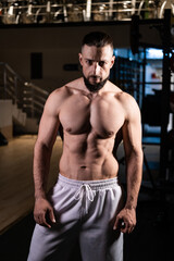 Fototapeta na wymiar A muscular man with a beard poses in the gym in white pants