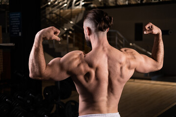 Fototapeta na wymiar Athletic man shows muscular back and arms in gym