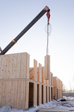 The construction process of a new modern modular house made of composite sip panels on a sunny winter day. A crane lifts one of the panels