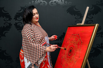 the artist draws a mandala with a brush and red paint on the canvas