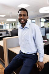 Vertical image of happy african american businessman looking at camera in office