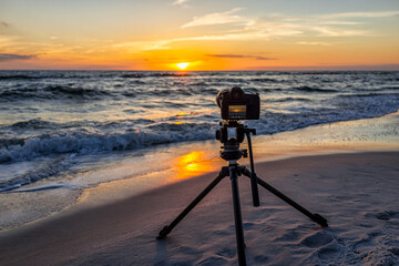 Professional camera and tripod filming colorful sunset and nobody in Gulf of Mexico coast with water waves in Seaside Santa Rosa Beach, Florida panhandle and reflection