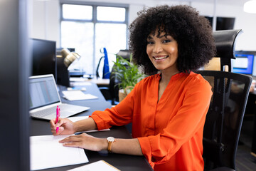 Happy african american businesswoman sitting at desk and smiling at camera