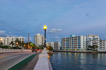 South Beach, Miami in evening blue hour night with condo apartment buildings in Florida and biscayne bay intracoastal canal water by street road - obrazy, fototapety, plakaty