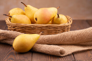 Fresh yellow pears in a basket, on burlap on a stone beige table.
