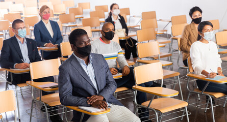 International group of business people wearing protective face masks listening to presentation in...