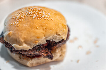 Small burger slider macro closeup with homemade thick hamburger patty on sesame seed bun white...