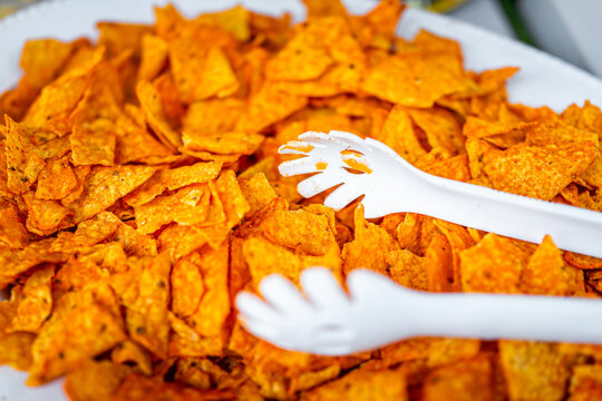 Macro closeup of corn spicy cheesy orange tortilla chips in bowl plate with texture at party with plastic tongs