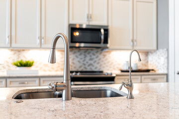 New modern faucet and kitchen sink closeup with island and granite countertops with bokeh...