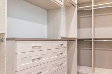 Spacious walk-in closet shelves, chest of drawers in modern minimalist white style in staging model house apartment bedroom
