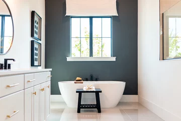 Bathtub in bathroom staging model home house or hotel with modern luxury white cabinets interior, window with light and mirrors © Kristina Blokhin