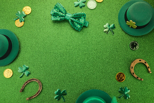 St Patricks Day frame of shamrocks, gold coins and leprechaun hat over a glittery green background
