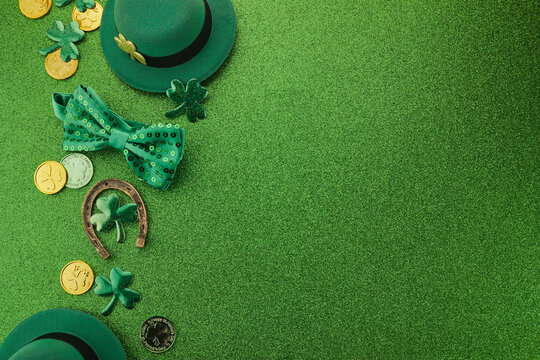 St Patricks Day frame of shamrocks, gold coins and leprechaun hat over a glittery green background