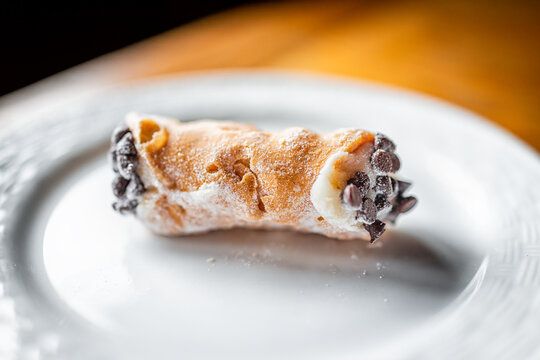 Italian cannolo pastry dessert closeup on white plate macro with texture of yellow crust and buttercream filling with chocolate chips in cannoli