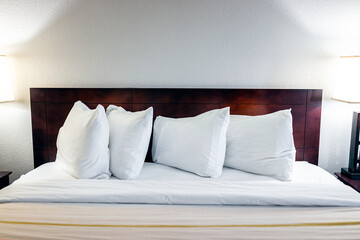 Fototapeta na wymiar Bedroom room with illuminated lit lamp light and front view of white pillows with sheets on empty mattress bed headboard in modern hotel with nobody