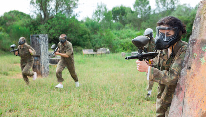 Fototapeta premium Asian female paintball player in protective mask and with gun on paintball field
