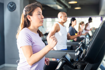 Young adult woman doing cardio workout running on treadmill at fitness center