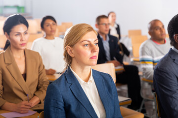 Portrait of young adult female attentively listening to motivation lecture with colleagues at conference