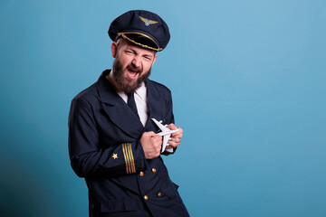 Funny pilot in uniform playing with small airplane model, aviation academy aviator holding...