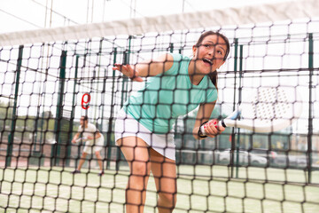 Portrait of emotional woman paddle tennis player during friendly doubles couple match at court, view through net