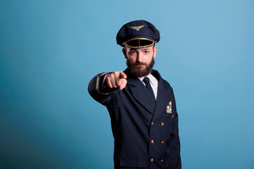 Serious airplane pilot pointing at camera, plane captain wearing uniform and hat front view...