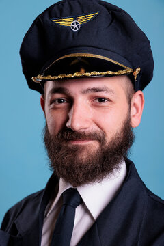 Aircraft captain wearing uniform and hat portrait, confident plane pilot standing with crossed arms, looking at camera. Smiling civil aviator with badge on professional suit