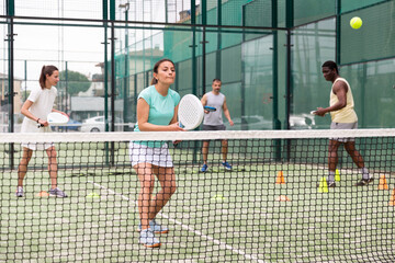 Happy woman learning to play padel game on tennis court outdoor. Other athletes are training in the...