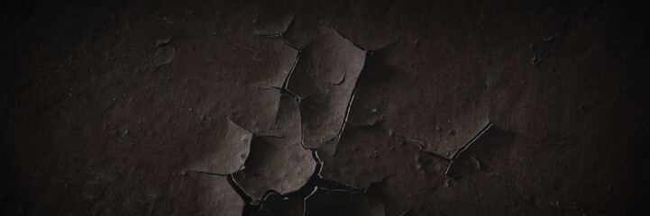 Dark wide panoramic background. Peeling paint on a concrete wall. Dark grunge texture of old cracked flaking paint. Weathered rough painted surface. Patterns of cracks. Darkness background for design.